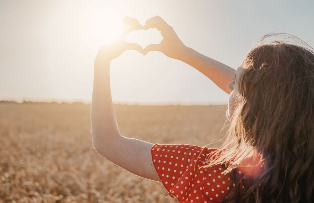 Frau formt Herz mit den Händen in der Sonne auf einem Feld