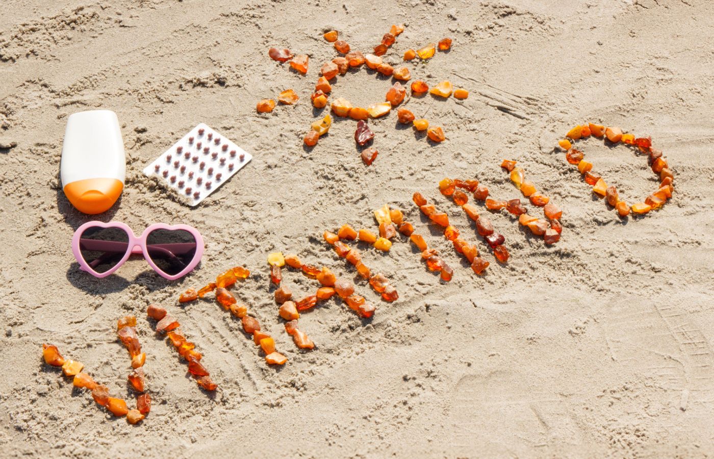 Vitamin-D-Schriftzug aus Karotten am Strand mit Sonnencreme und Sonnenbrille