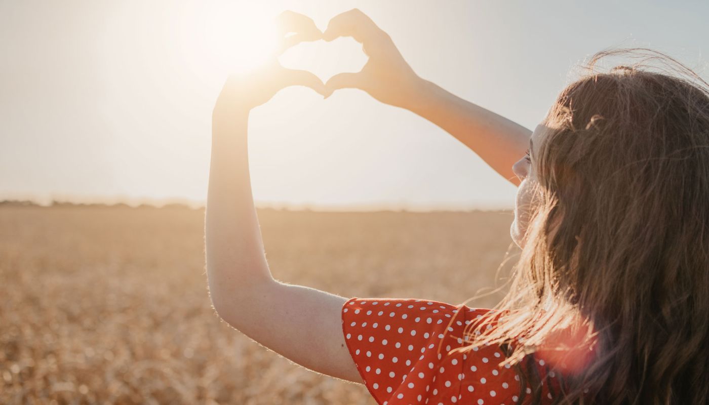 Frau formt Herz mit den Händen in der Sonne auf einem Feld