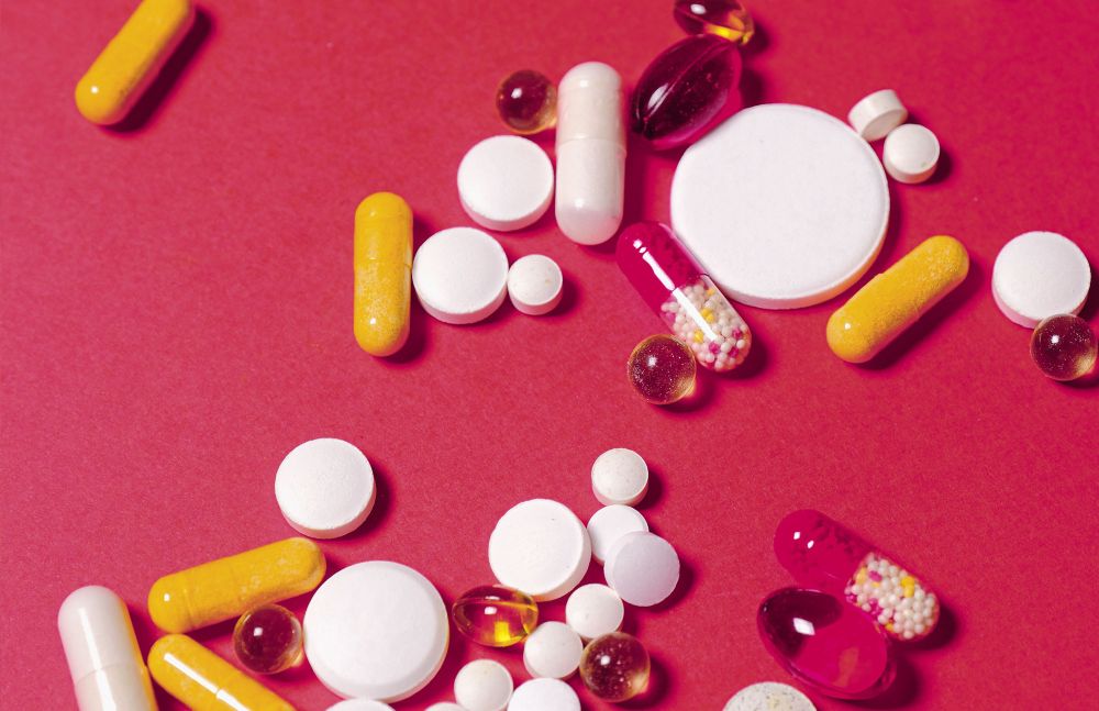 Verschiedene bunte Tabletten und Kapseln auf rotem Hintergrund