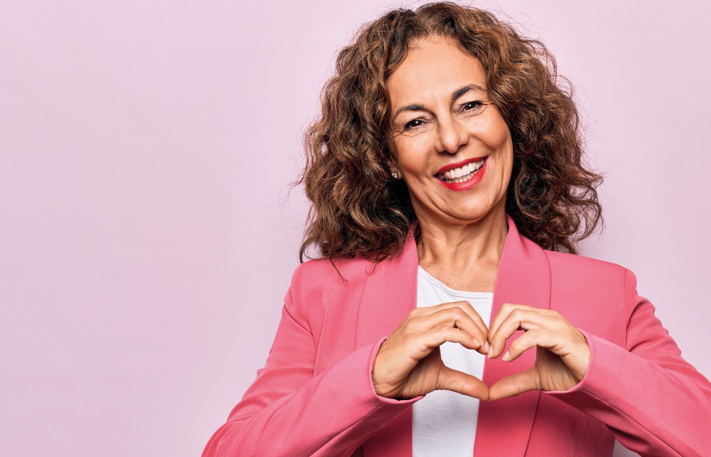 Frau formt mit den Händen ein Herz vor rosa Hintergrund