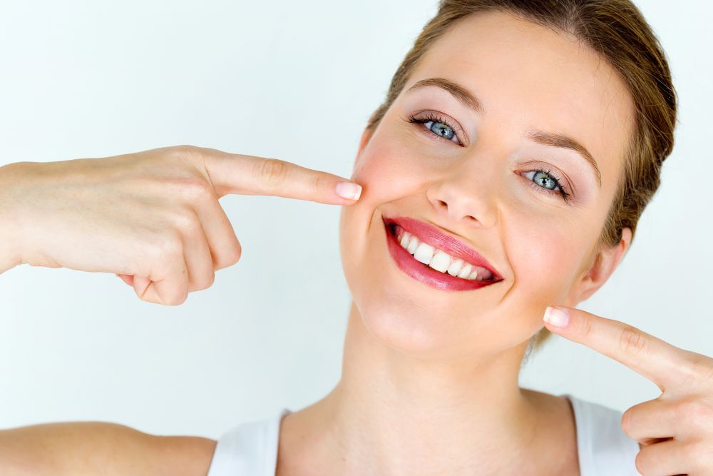 Frau zeigt lachend auf ihre weißen Zähne