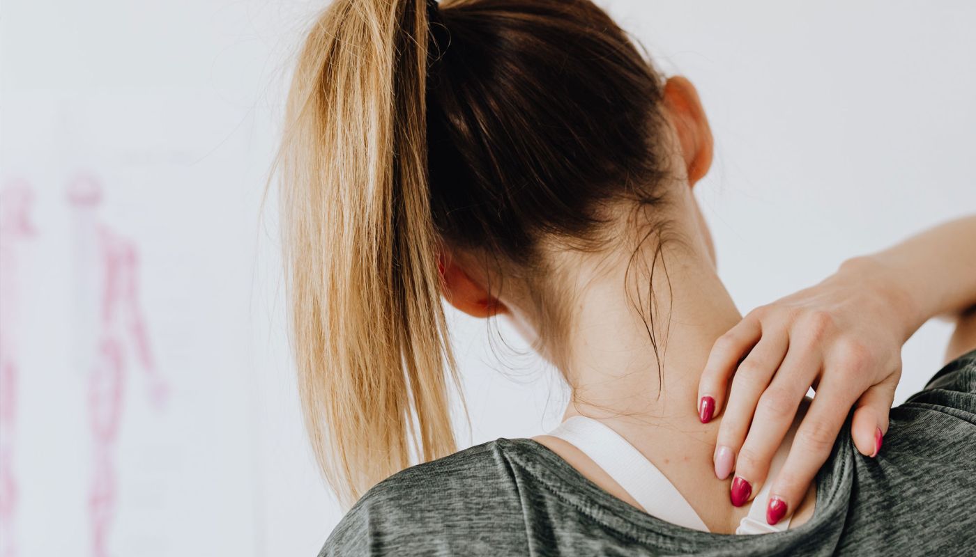 Frau mit Pferdeschwanz greift sich an die Schulter
