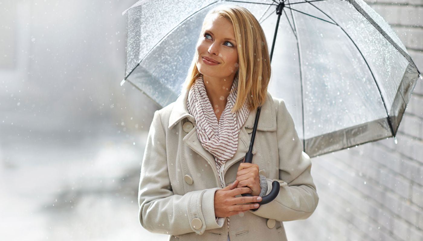 Frau mit Regenschirm im Regen lächelt in die Kamera