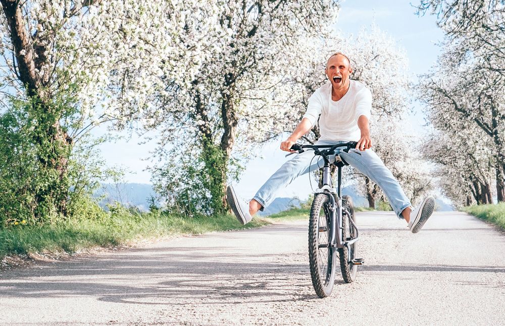 Mann fährt fröhlich mit dem Fahrrad auf blühender Allee