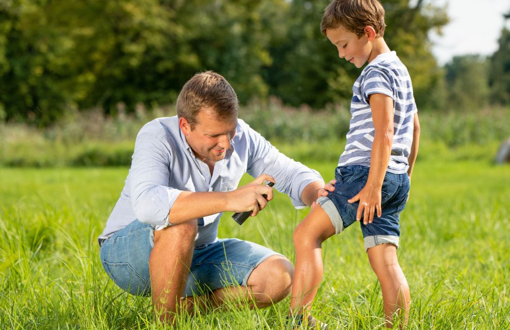 Vater sprüht Insektenschutz auf das Bein seines Kindes im Freien
