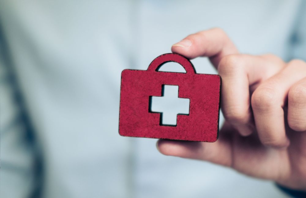 Hand hält rote Symbolfigur in Form einer Hausapotheke mit weißem Kreuz