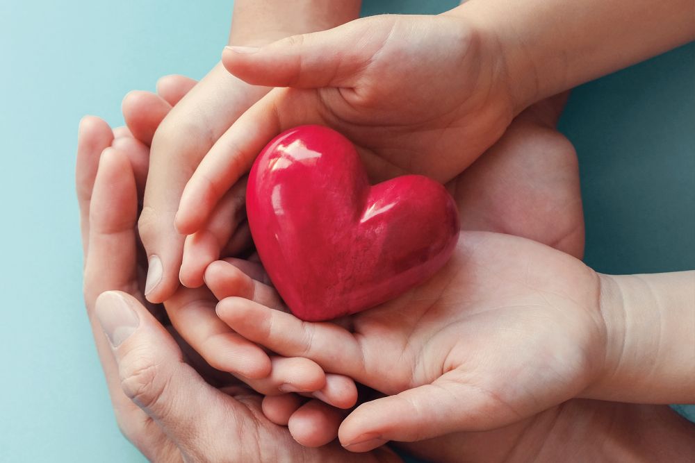 Zwei Kinderhände halten ein rotes Herz in den Händen eines Erwachsenen