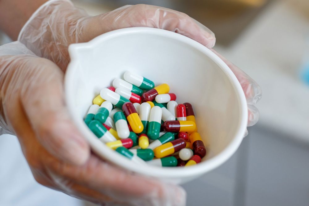 Hände in Handschuhen halten Schale voller bunter Tabletten
