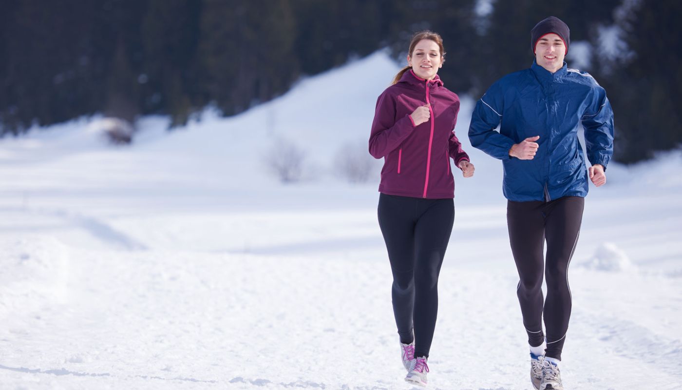 Frau und Mann joggen im Schnee bei sonnigem Winterwetter
