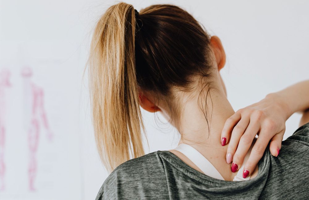 Frau mit Pferdeschwanz greift sich an die Schulter