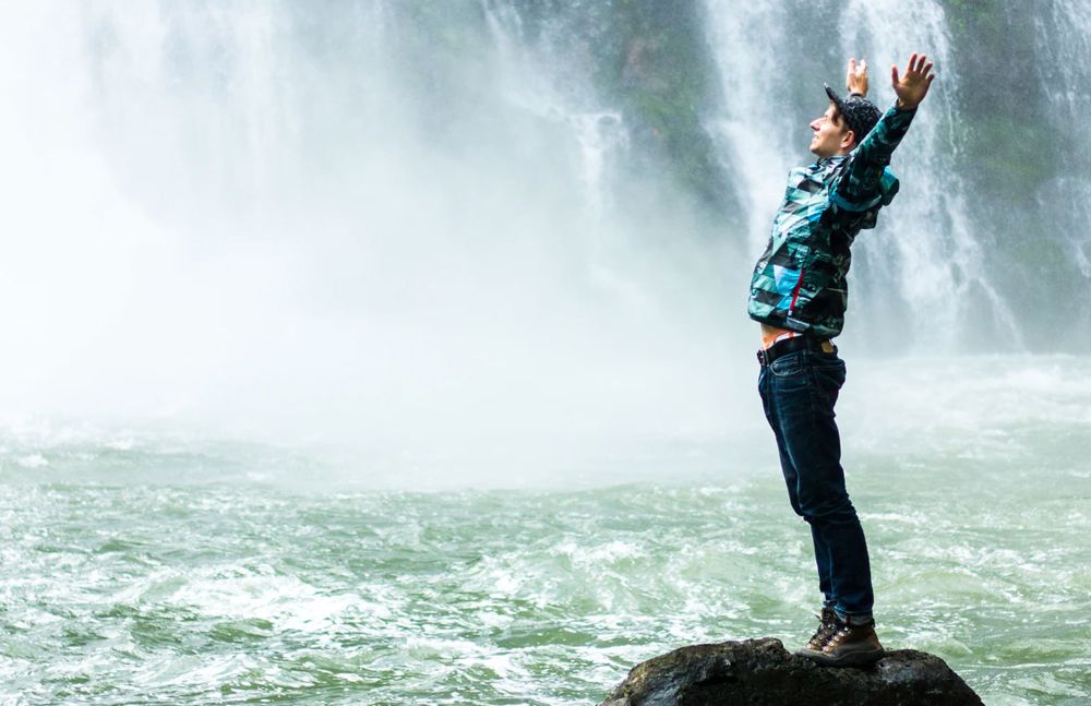 Mann steht vor Wasserfall mit erhobenen Armen