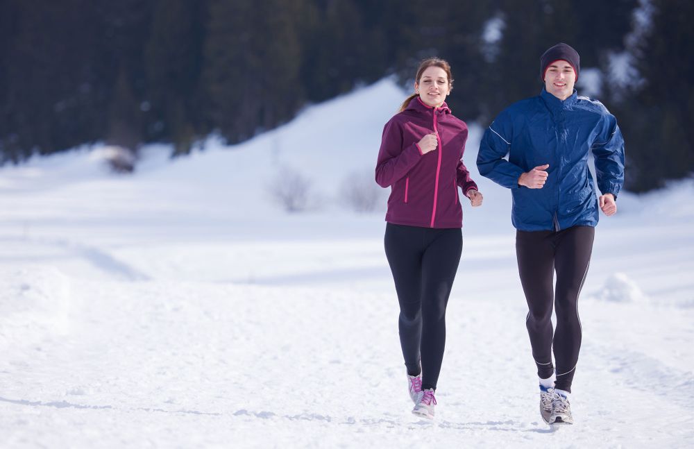 Frau und Mann joggen im Schnee bei sonnigem Winterwetter