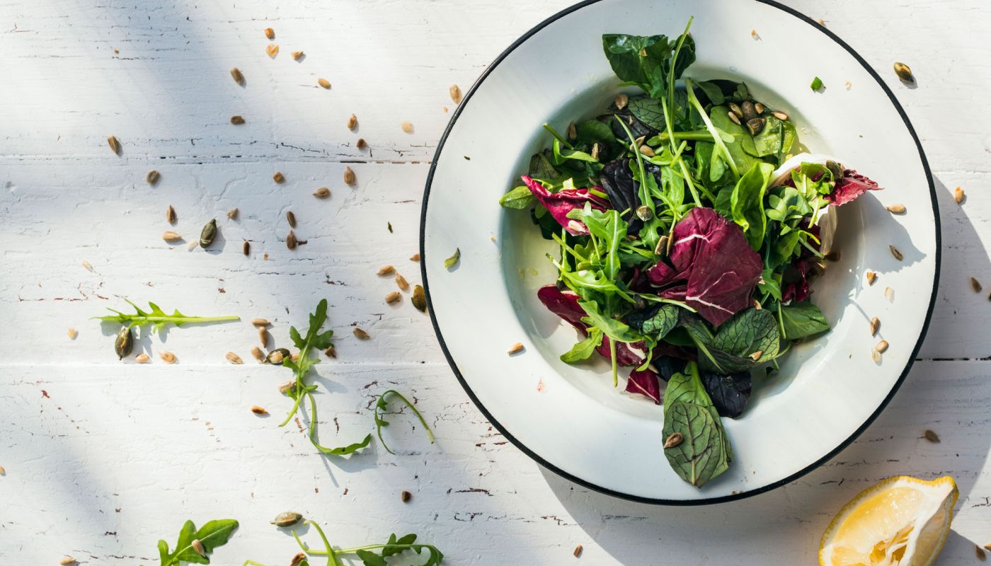 Bunter Blattsalat in weißem Teller auf hellem Holztisch