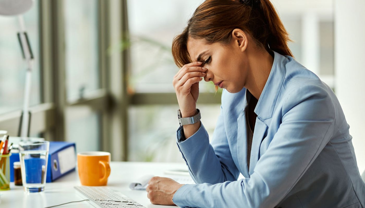 Frau am Schreibtisch stützt den Kopf in die Hand und wirkt erschöpft