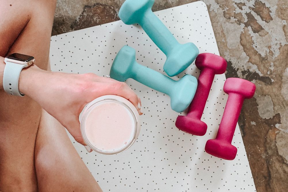 Frau mit Sportgetränk und Hanteln auf dem Boden