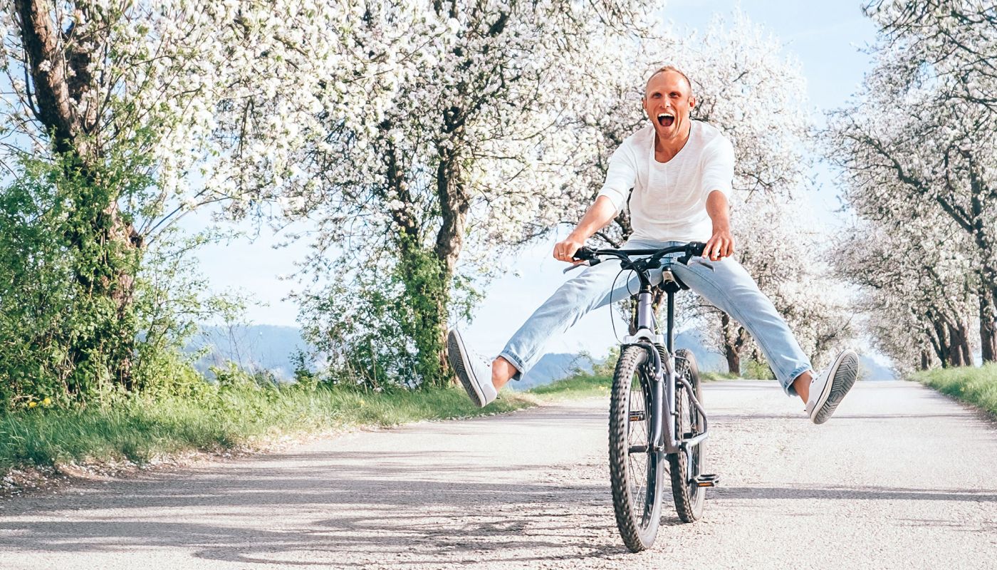 Mann fährt fröhlich mit dem Fahrrad auf blühender Allee