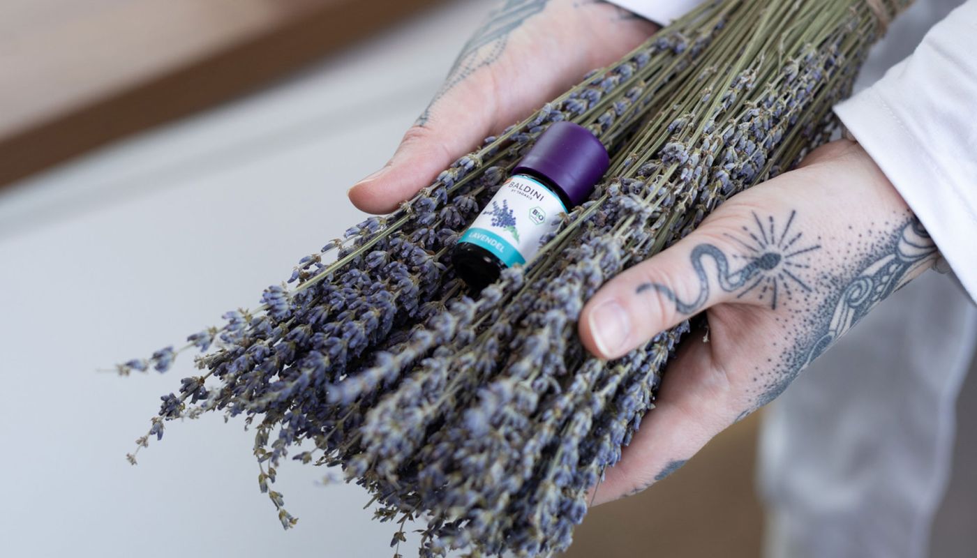 Hände halten Lavendelstrauß und ätherisches Ölfläschchen