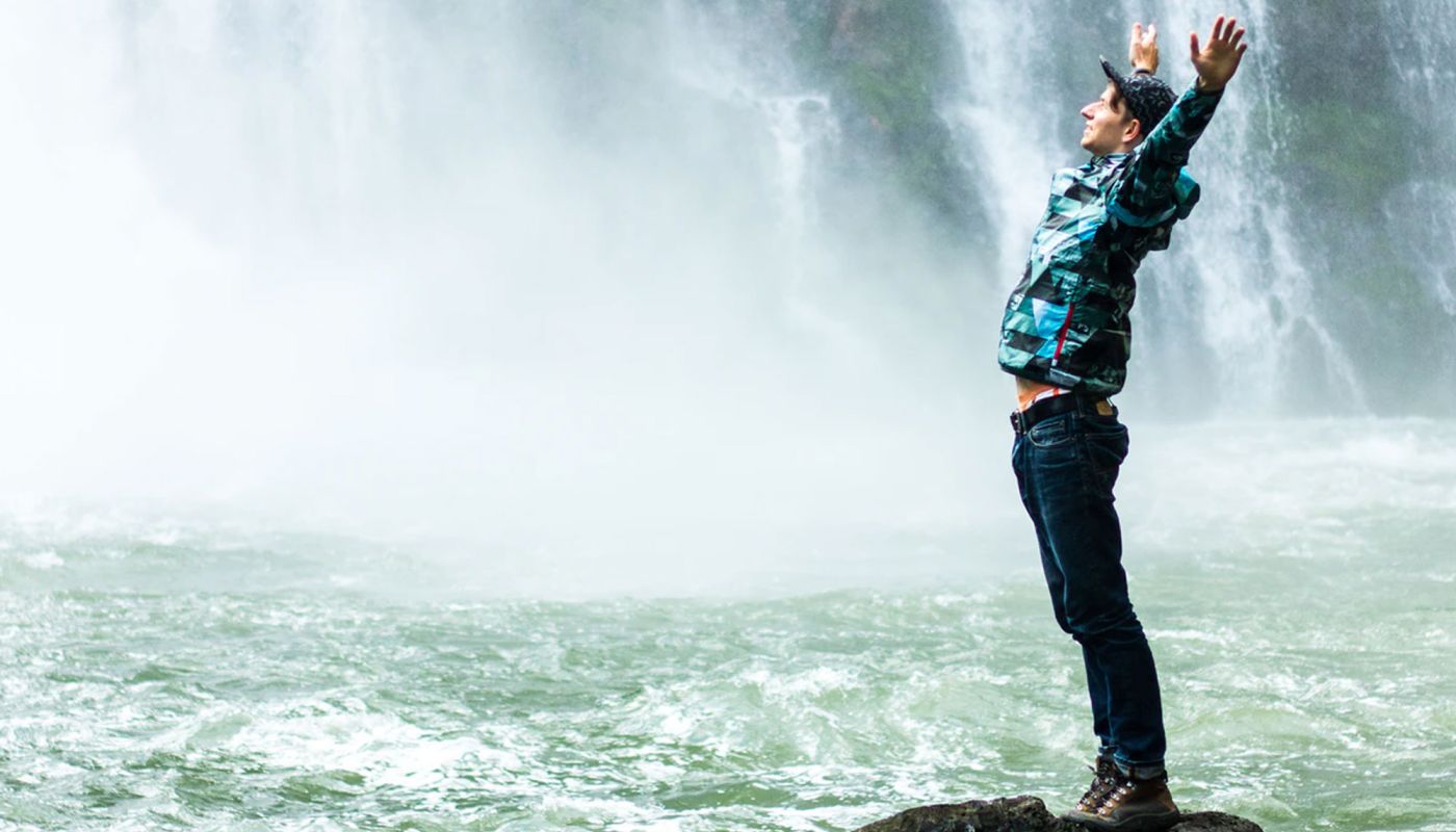 Mann steht vor Wasserfall mit erhobenen Armen