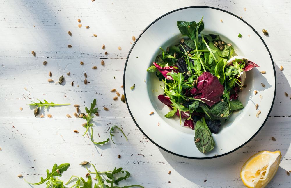 Bunter Blattsalat in weißem Teller auf hellem Holztisch
