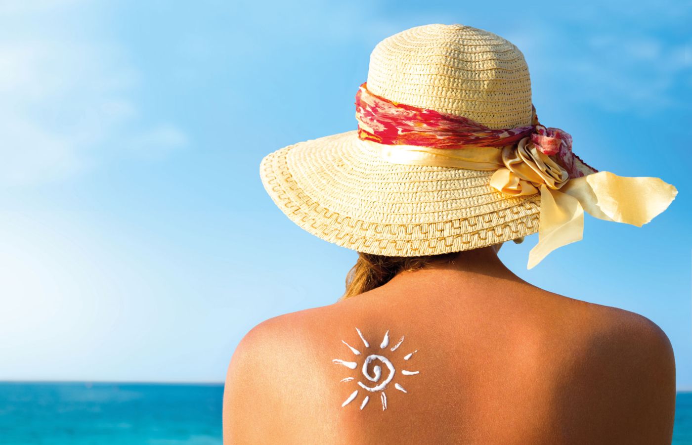 Frau mit Sonnenhut zeigt Sonnencreme-Symbol auf Rücken