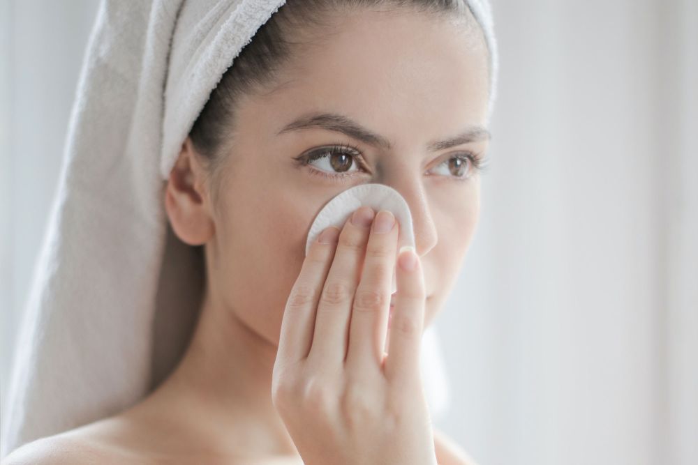 Junge Frau mit Handtuch tupft sich das Gesicht mit Wattepad