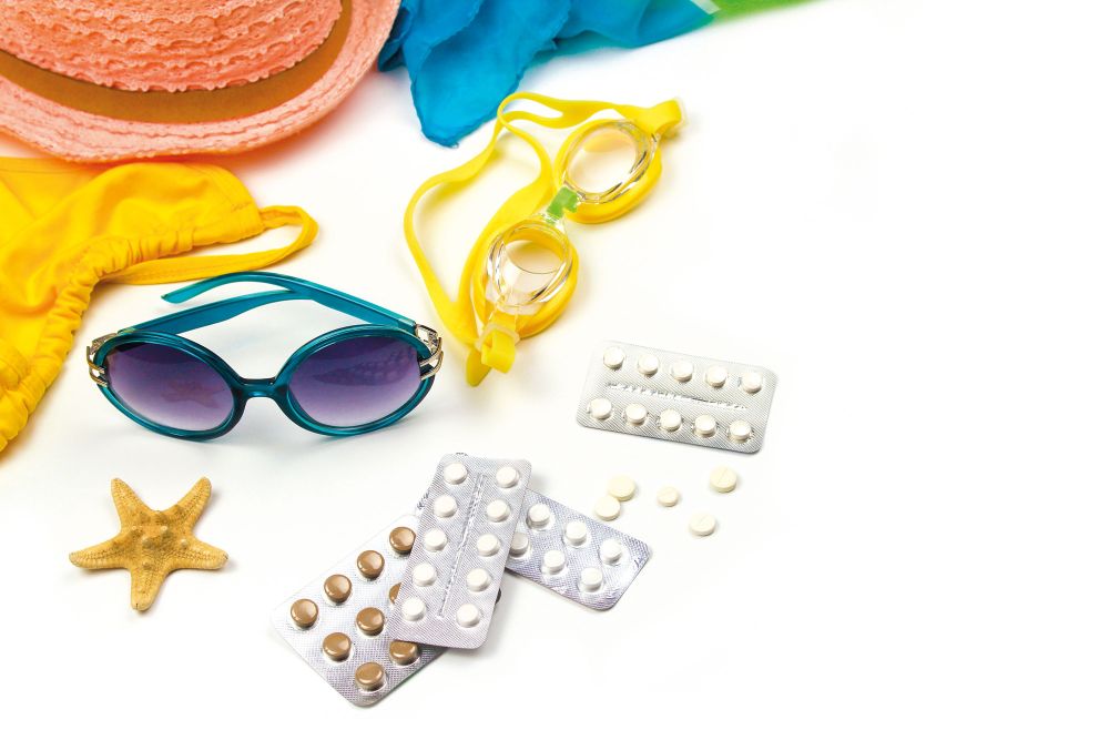 Urlaubsgegenstände wie Sonnenbrille, Bikini, Medikamente auf Tisch