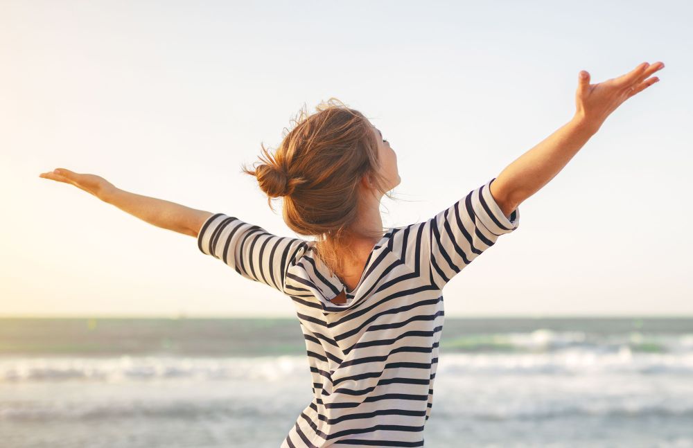 Frau am Strand breitet glücklich die Arme aus