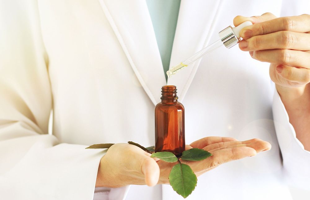 Apothekerin träufelt ätherisches Öl aus einer Pipette in eine braune Flasche