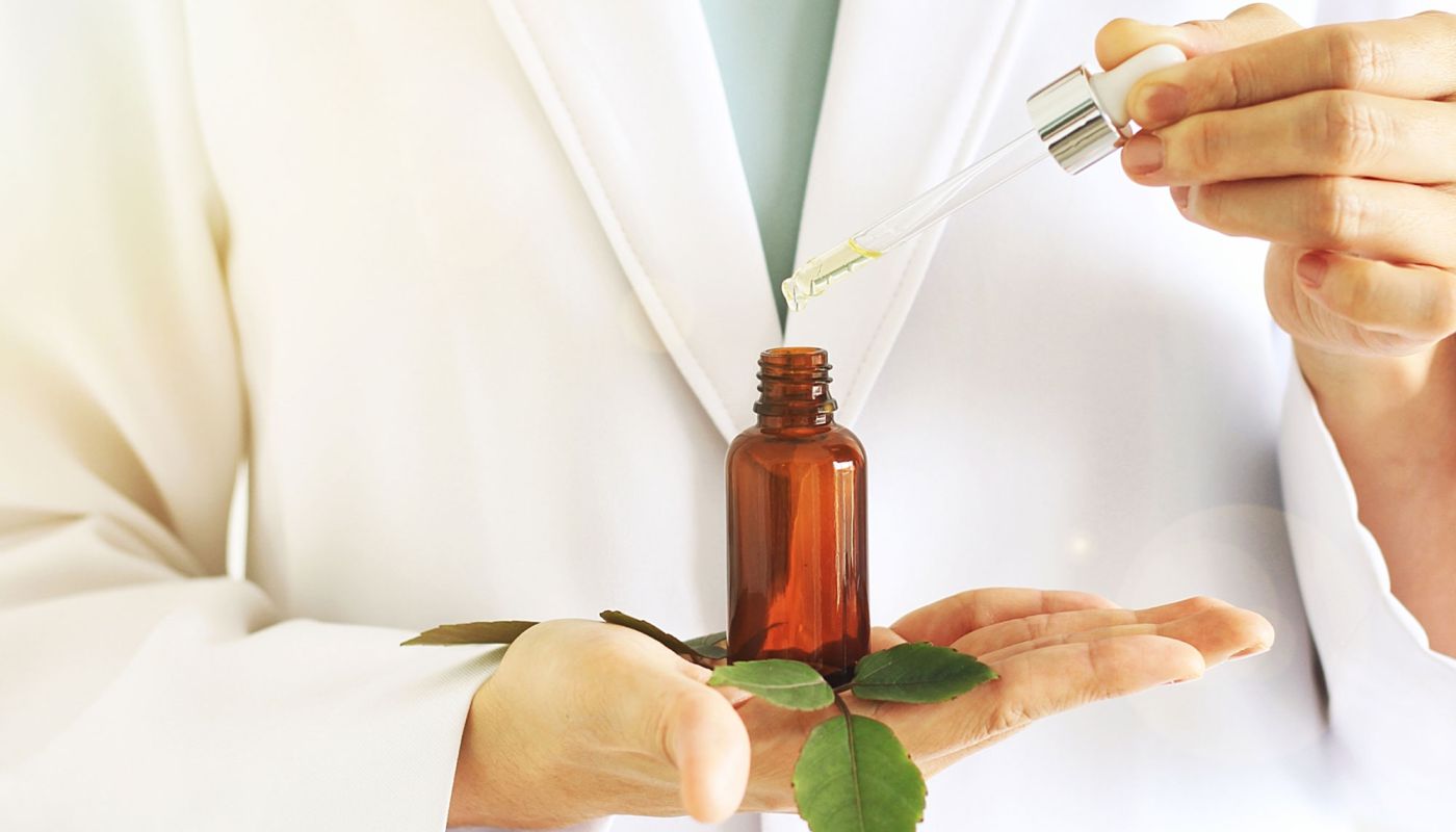 Apothekerin träufelt ätherisches Öl aus einer Pipette in eine braune Flasche
