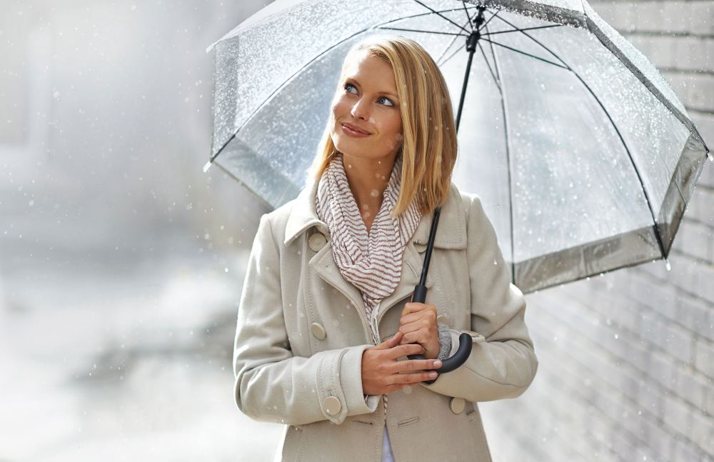 Frau mit Regenschirm im Regen lächelt in die Kamera