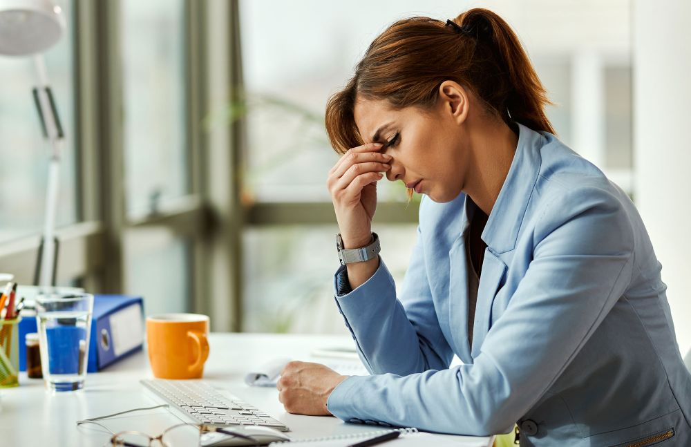 Frau am Schreibtisch stützt den Kopf in die Hand und wirkt erschöpft