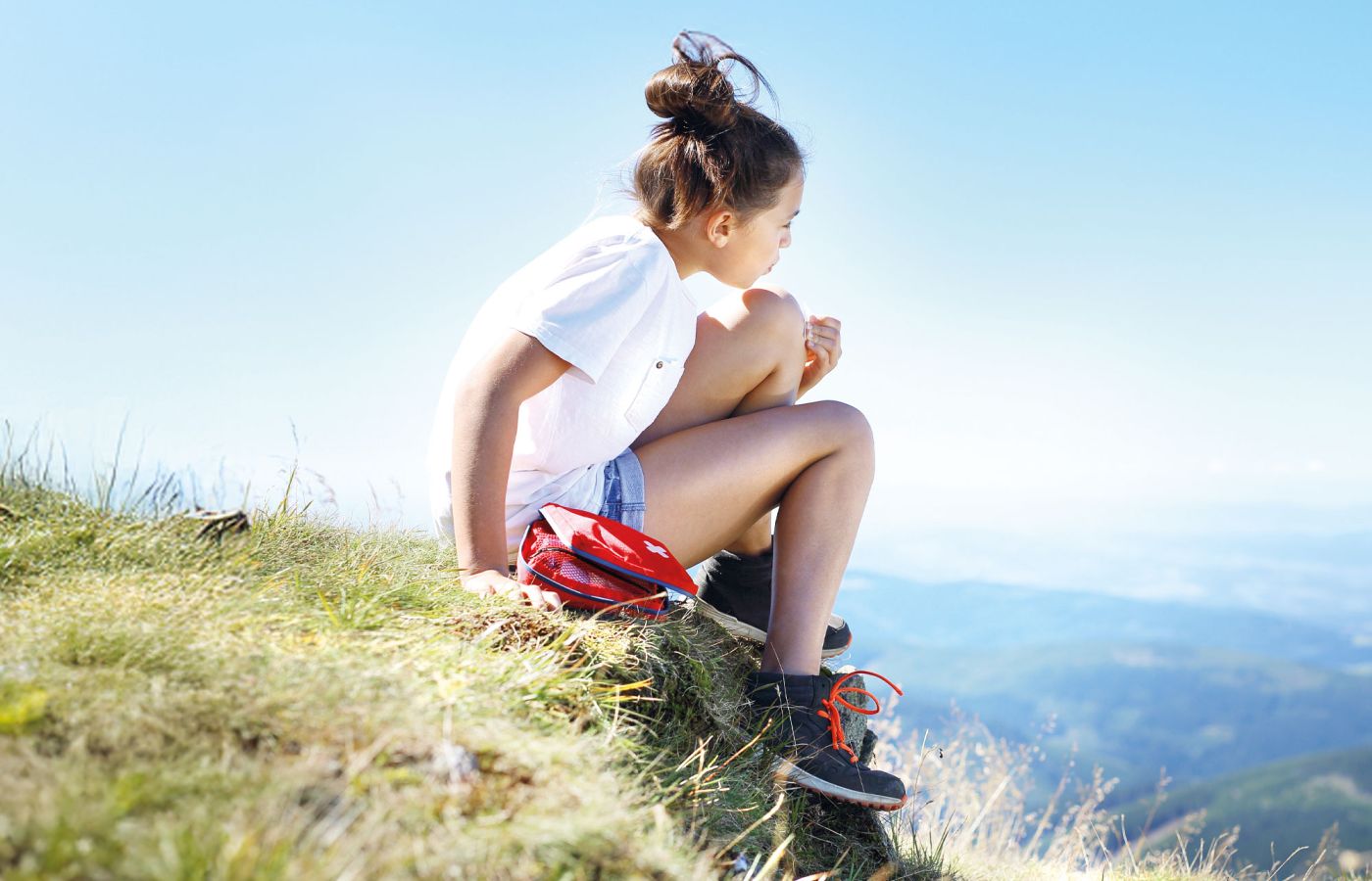 Mädchen sitzt mit Rucksack auf Bergwiese