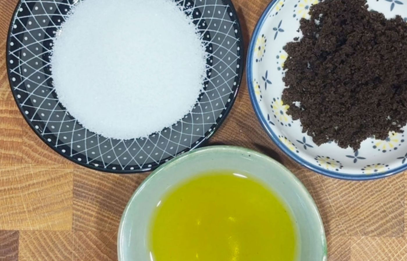 Schalen mit Zucker, gemahlenem Kaffee und Öl auf Holzbrett, Draufsicht.