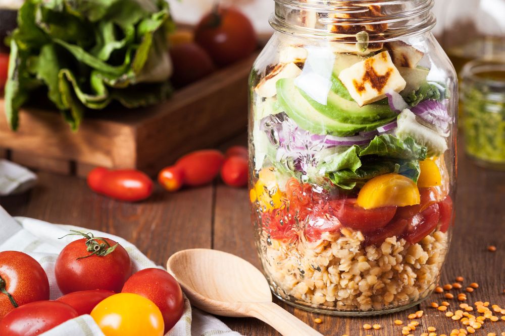 Einmachglas mit buntem Schichtsalat und frischem Gemüse daneben