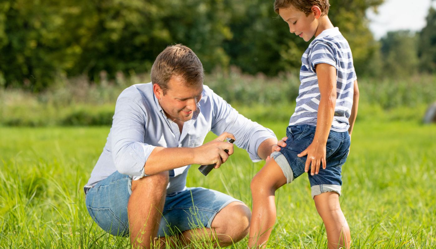 Vater sprüht Insektenschutz auf das Bein seines Kindes im Freien