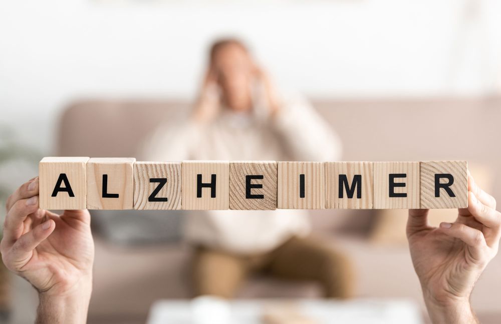 Holzbuchstaben bilden das Wort Alzheimer, unscharfe Person im Hintergrund