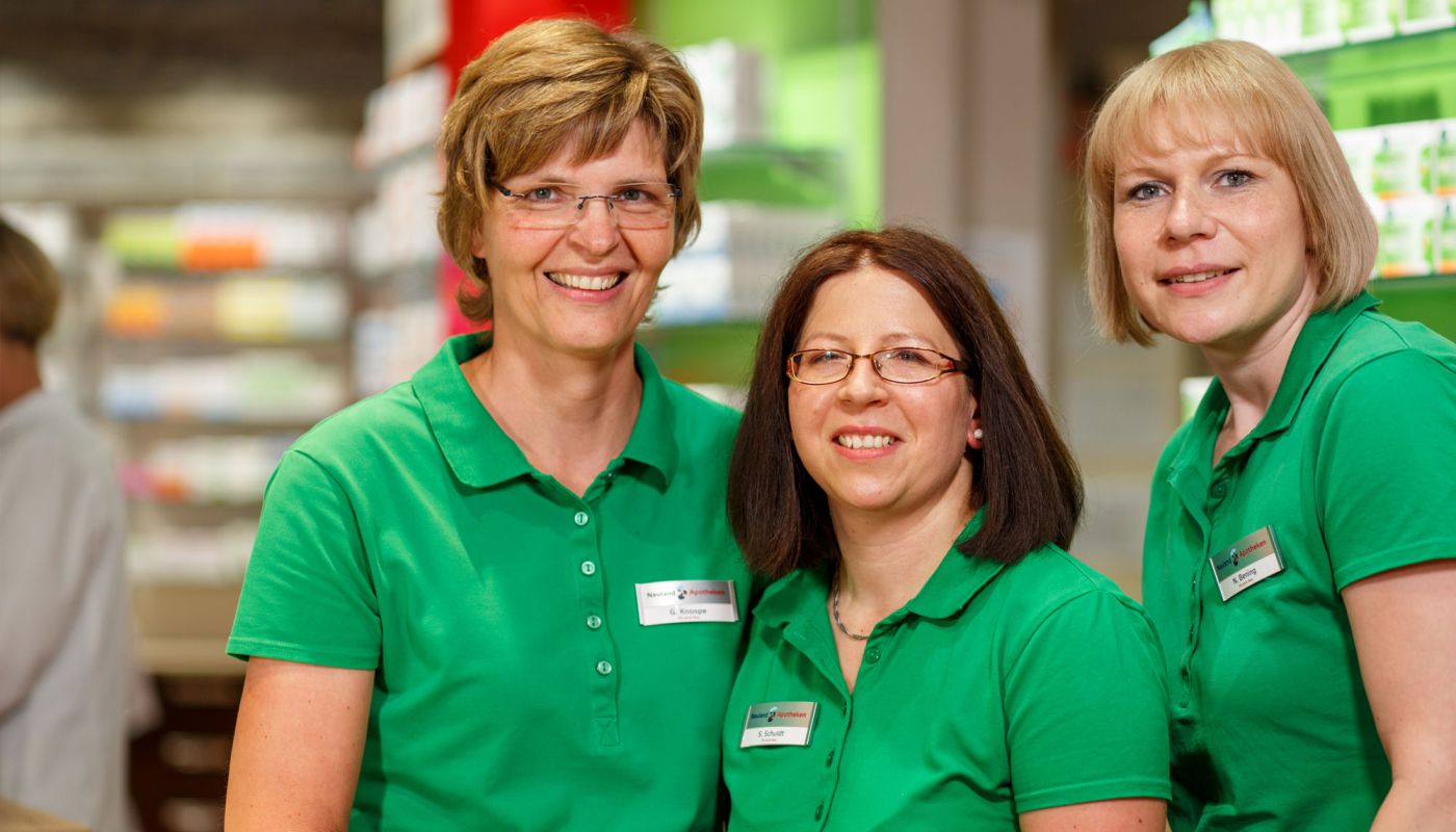 Drei Apothekerinnen in grünen Shirts lächeln in die Kamera