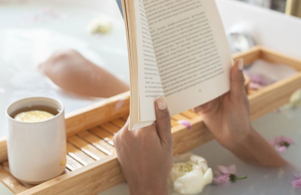 Person liest entspannt ein Buch in der Badewanne mit Teetasse daneben