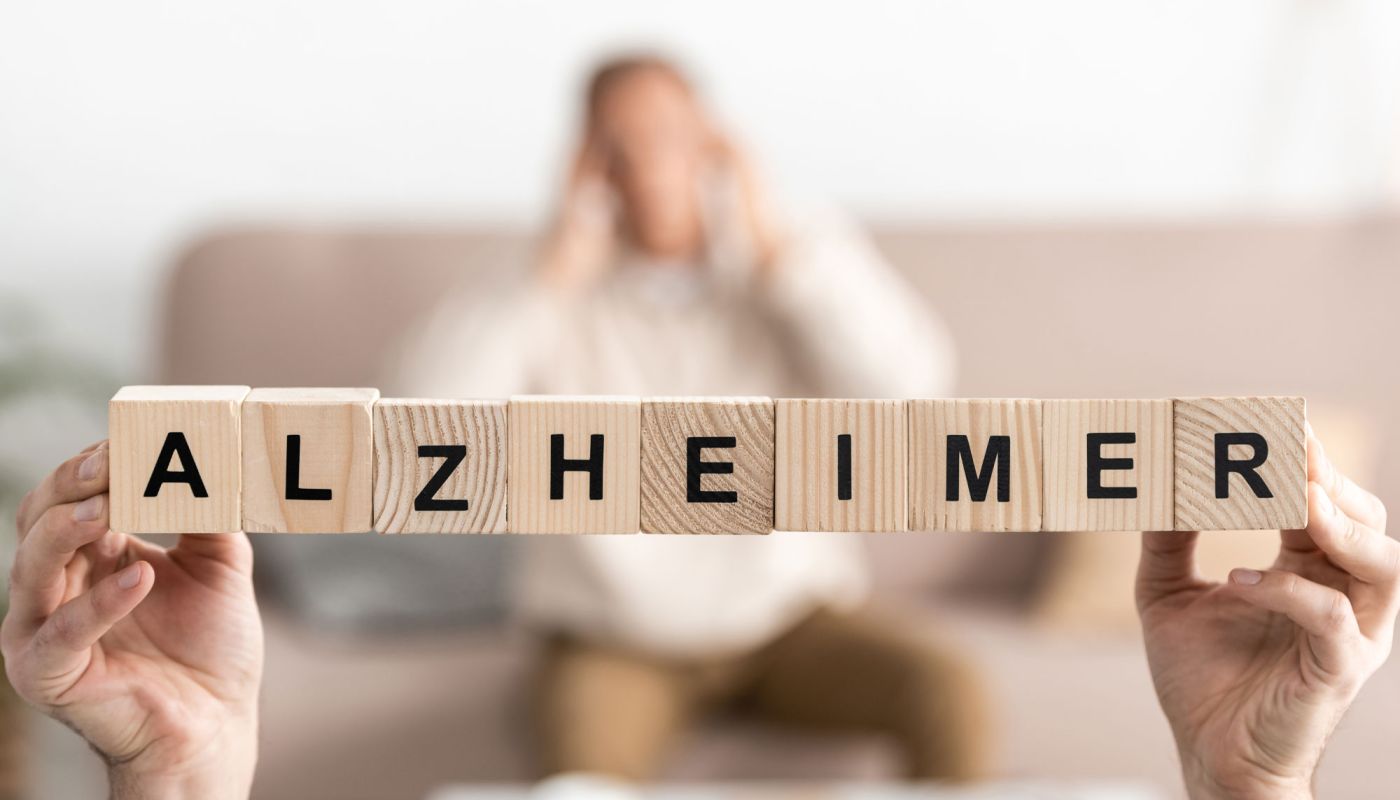 Holzbuchstaben bilden das Wort Alzheimer, unscharfe Person im Hintergrund