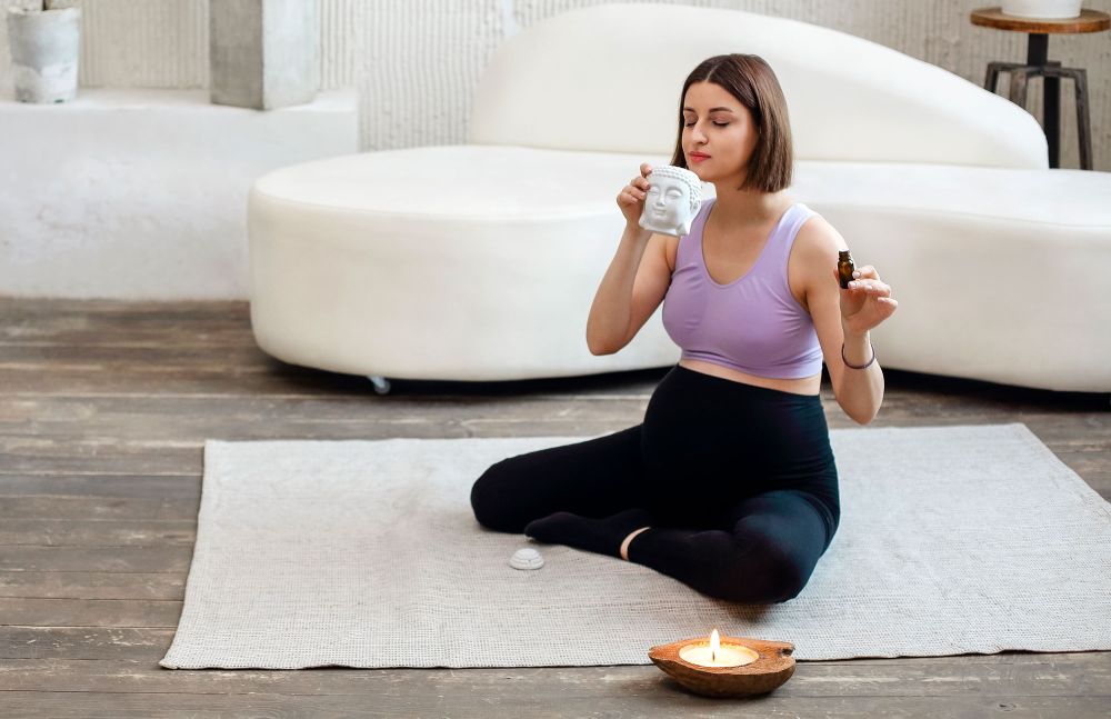 Schwangere Frau sitzt im Schneidersitz auf Yogamatte und riecht an einem Aromaöl