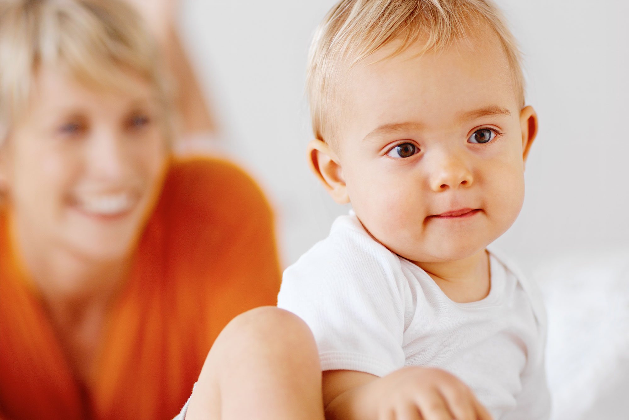 Baby sitzt lachend auf Schoß der Mutter