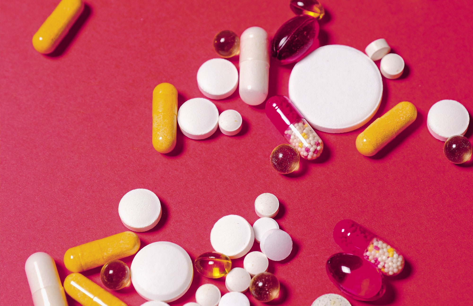 Verschiedene bunte Tabletten und Kapseln auf rotem Hintergrund