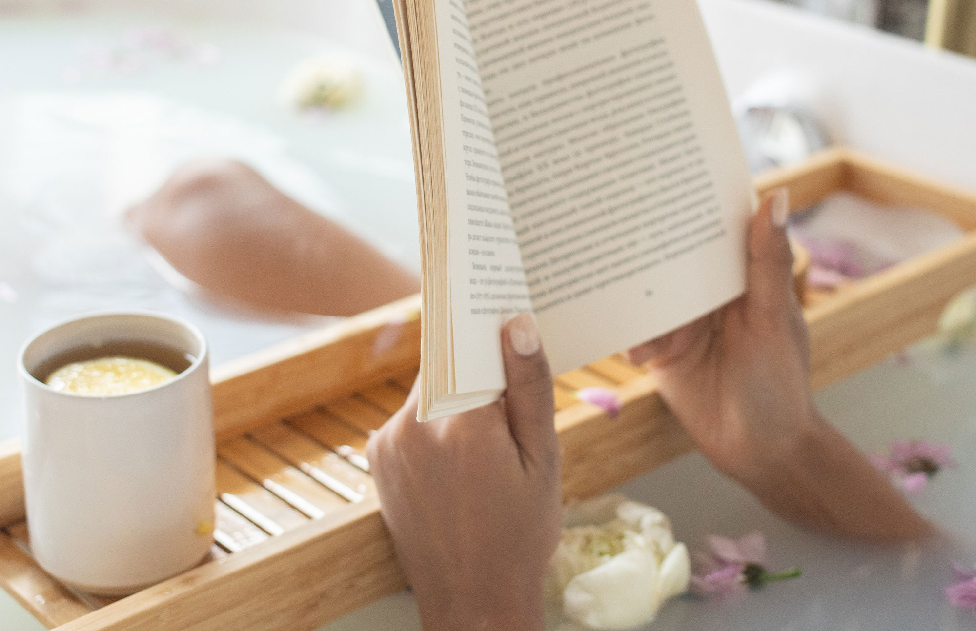 Person liest entspannt ein Buch in der Badewanne mit Teetasse daneben